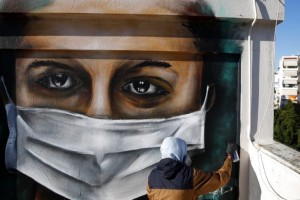 S.F., a 16-year-old Greek graffiti artist, spray-paints a design, a woman wearing a face mask referring to protection against coronavirus, on the roof of his apartment block in Athens, Tuesday, March 17, 2020. Greece has imposed a wide range of public safety measures to try and contain the coronavirus outbreak, including school and store closures. The vast majority of people recover from the new coronavirus. According to the World Health Organization, most people recover in about two to six weeks, depending on the severity of the illness. (AP Photo/Thanassis Stavrakis)
