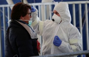A person wearing a protective suit and mask checks the temperature of people departing from the ferry port of Molo Beverello after Italy orders a countrywide lockdown to try and contain a coronavirus outbreak, in Naples, Italy, March 10, 2020. REUTERS/Ciro De Luca